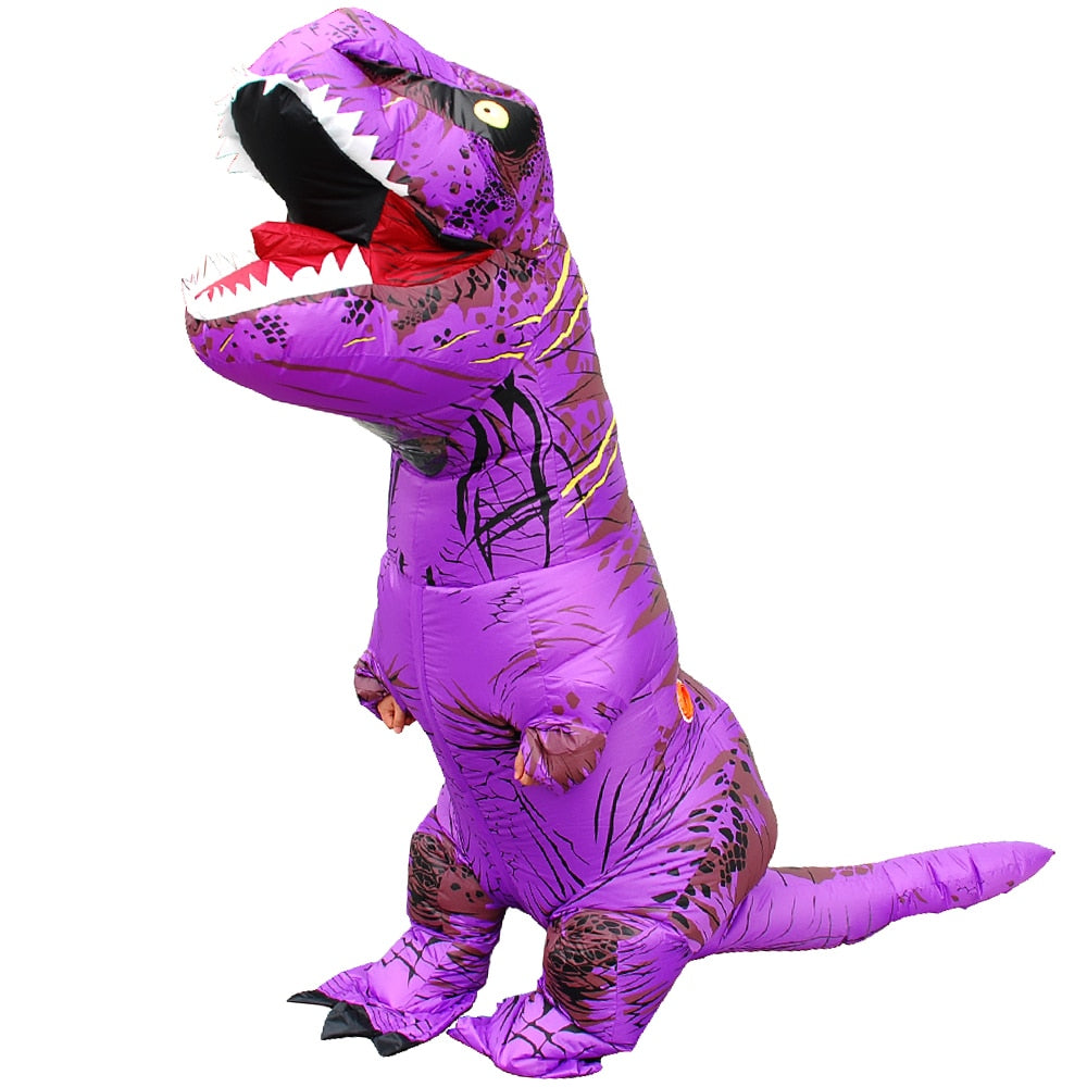 Personne portant un costume gonflable de dinosaure de couleur violette, avec une grande tête de dinosaure, des bras et des jambes courts, et une queue. Le costume est orné de nuances de violet, créant un aspect inhabituel pour un dinosaure. La personne à l'intérieur du costume affiche un sourire et semble prête à s'amuser lors d'un événement festif ou d'une fête costumée.